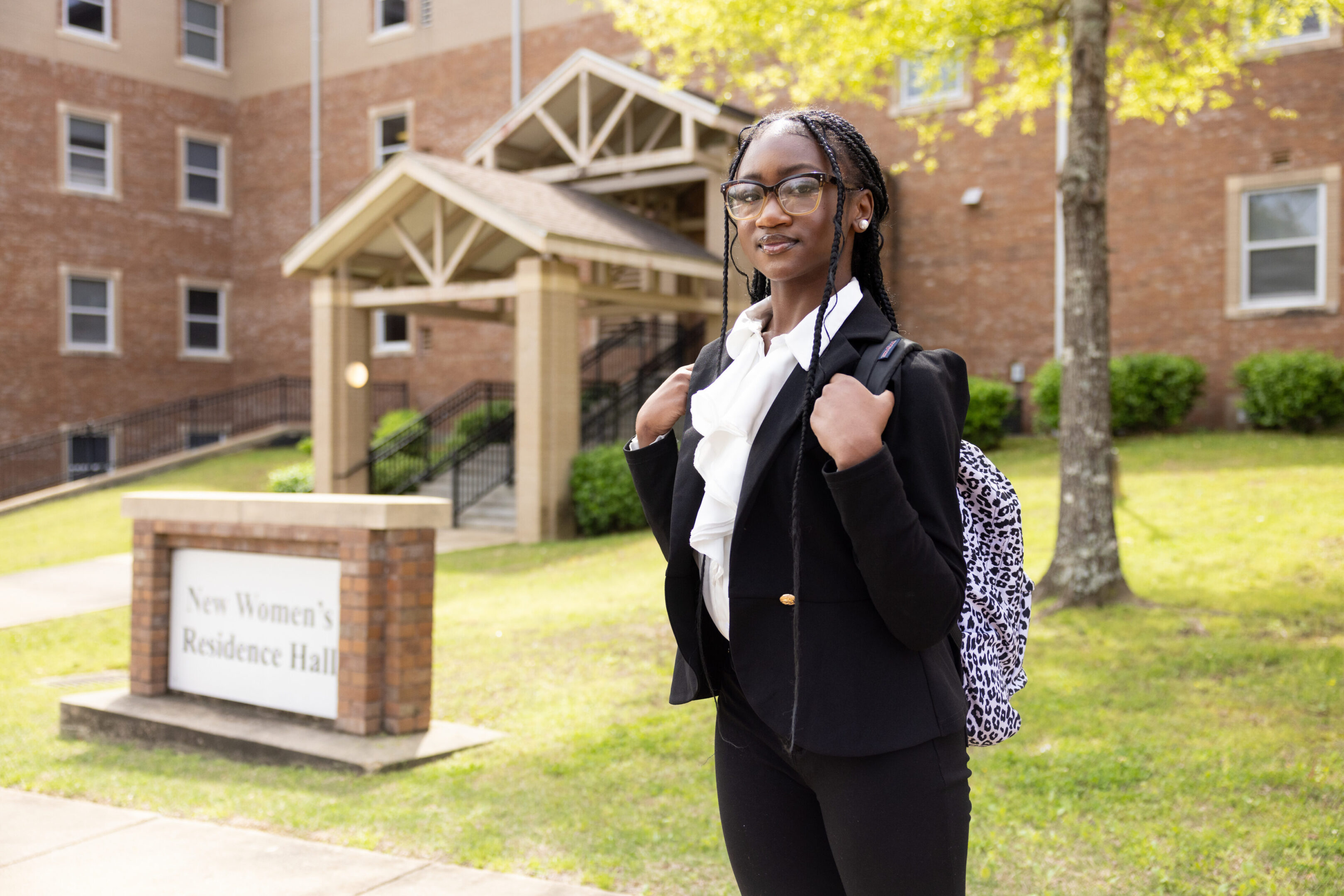 A confident student stands outside a university building with a backpack.