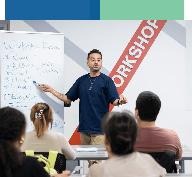 A man leading a workshop, pointing at a whiteboard with attendees listening.